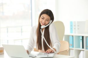 Woman talking by the telephone while working with laptop in office