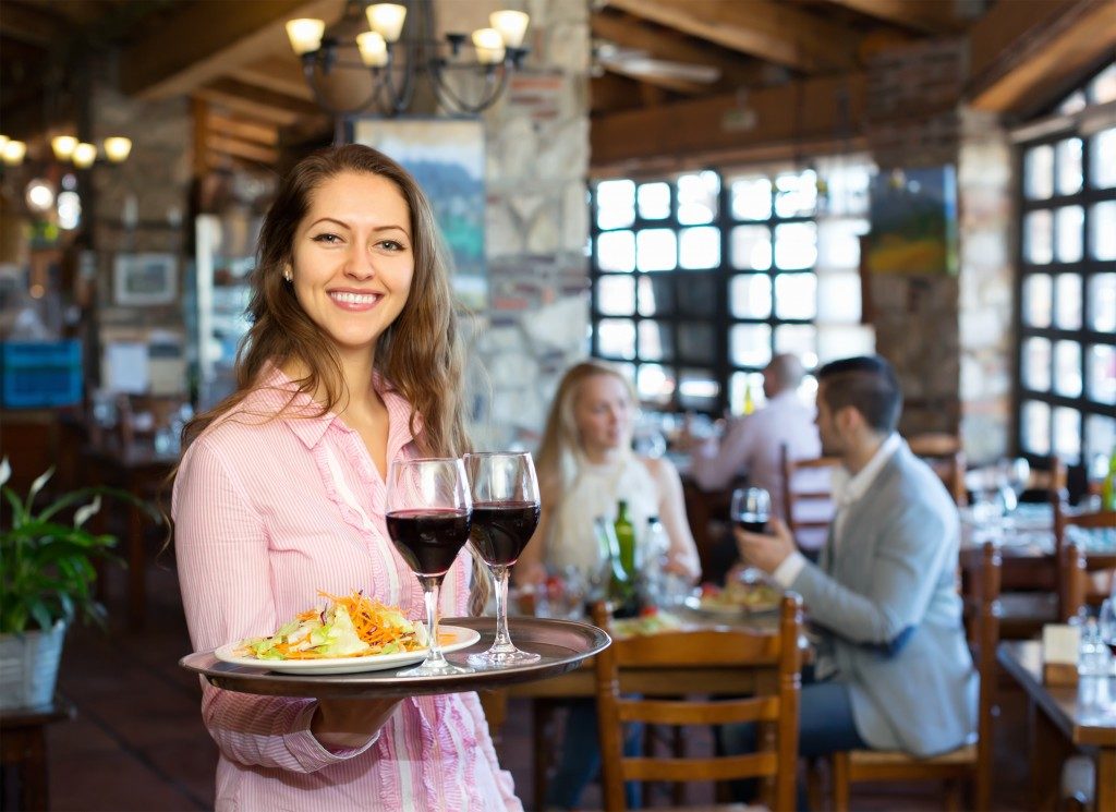 a woman holding a tray of red wines and a salad