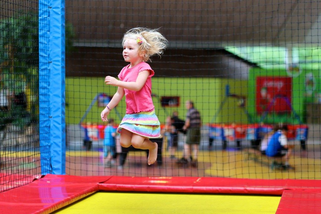 Little child jumping at trampoline in indoors playground. Active toddler girl having fun at sport centre.