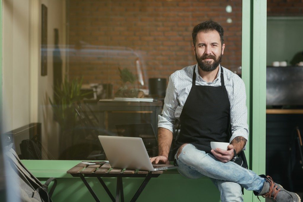 Businessman wearing apron while sitting beside laptop