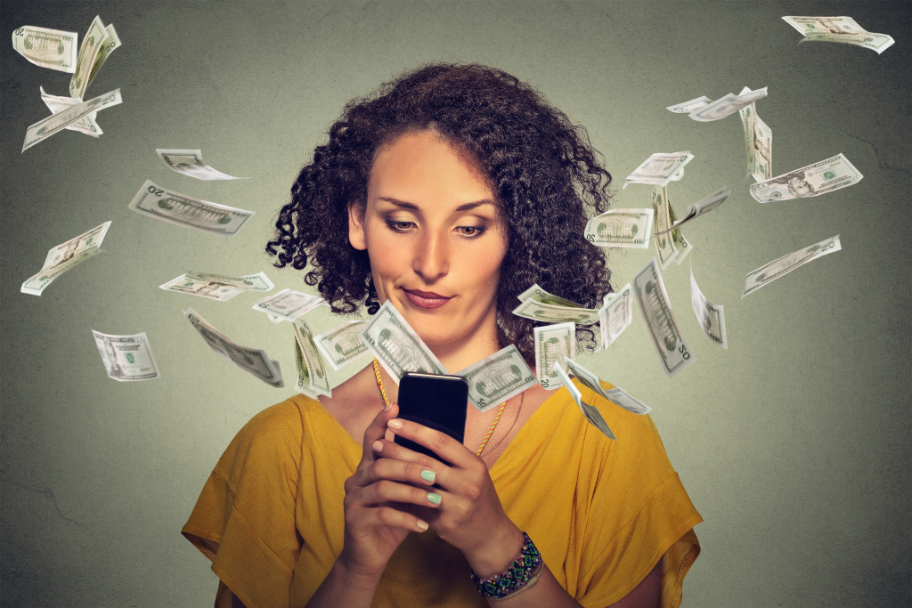 A woman using her phone while paper bills flies out of it