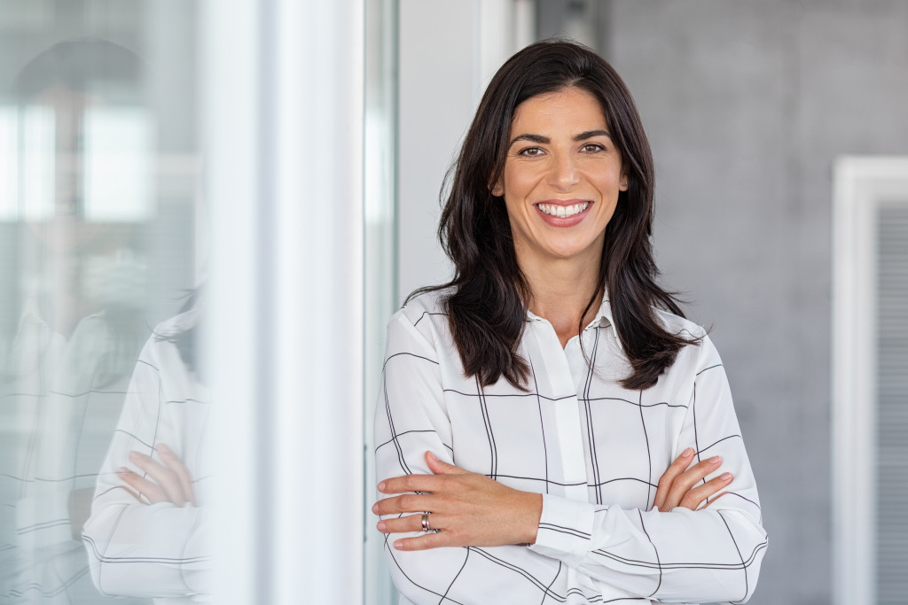 smiling businesswoman wearing neutral polo while standing near office glass
